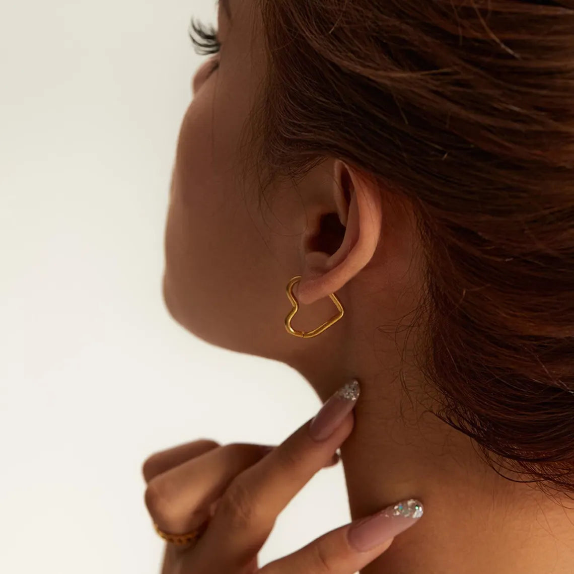 A woman showing off a geometric gold heart-shaped huggie hoop earring, styled with a minimalist aesthetic.
