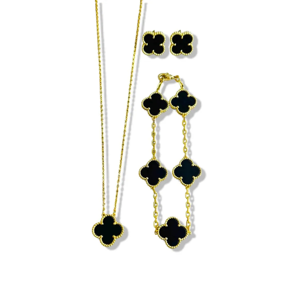An elegant 18K gold plated jewelry set featuring a black four-leaf clover necklace, matching bracelet, and stud earrings laid on a white background.