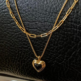 Close-up of a black heart pendant and layered gold chains on a black leather background, showcasing the high-shine 18K gold plating.
