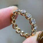 Gold ring with diamonds held between fingers against a neutral background