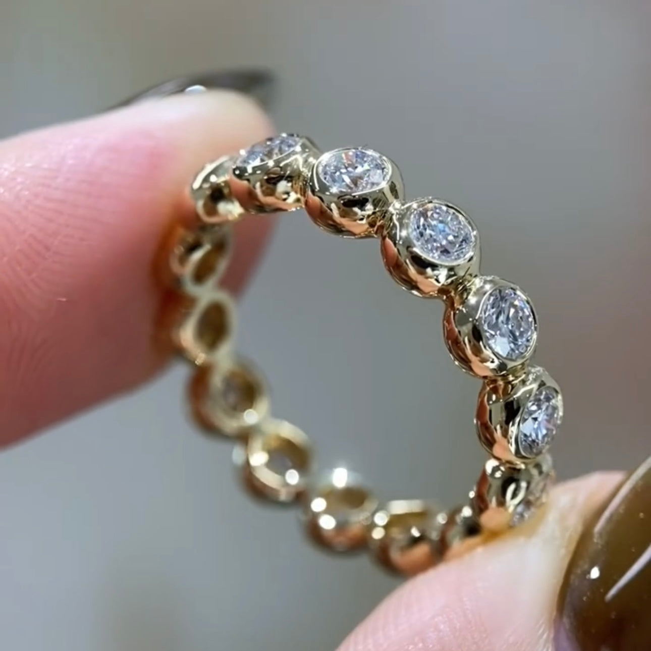 Gold ring with diamonds held between fingers against a neutral background