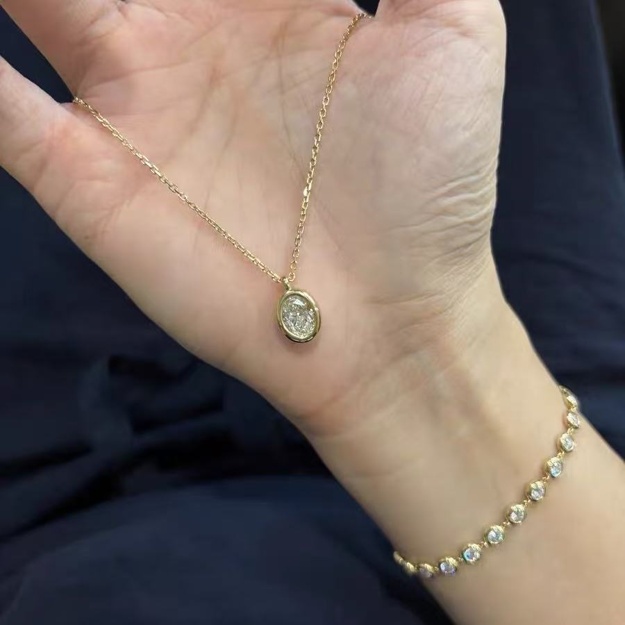A hand displaying the Bubble Luxe oval bezel necklace alongside a matching diamond tennis bracelet.