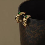 Close-up of the chunky 18K gold quilted hoops with vibrant gemstone accents hanging on the edge of a textured cup
