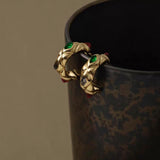 Close-up of the chunky 18K gold quilted hoops with vibrant gemstone accents hanging on the edge of a textured cup