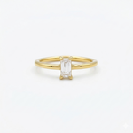 A classic minimalist gold solitaire ring featuring a clear emerald-cut cubic zirconia set vertically, isolated on a clean white background.