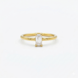 A classic minimalist gold solitaire ring featuring a clear emerald-cut cubic zirconia set vertically, isolated on a clean white background.