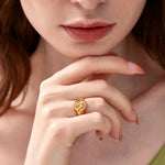 Close-up of a woman resting her chin on her hand, highlighting a gold signet ring with a cherub motif on her middle finger.