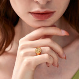 Close-up of a woman resting her chin on her hand, highlighting a gold signet ring with a cherub motif on her middle finger.