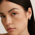 Close-up of a woman's face highlighting the sparkling 3-stone silver huggie earring hugging her earlobe perfectly.