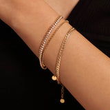 Close-up of a woman's wrist modeling a delicate 18K gold plated bracelet that gives the illusion of three stacked chains, including two beaded rows and one sparkling cubic zirconia row.