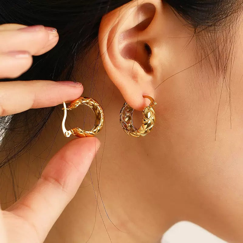 Detailed close-up of a model holding and wearing 18K gold quilted hoops, showing the secure clasp and high-shine finish.