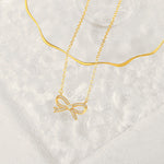 A beautifully crafted gold pave bow necklace draped elegantly over a textured clear glass aesthetic display tray.