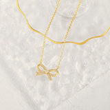 A beautifully crafted gold pave bow necklace draped elegantly over a textured clear glass aesthetic display tray.