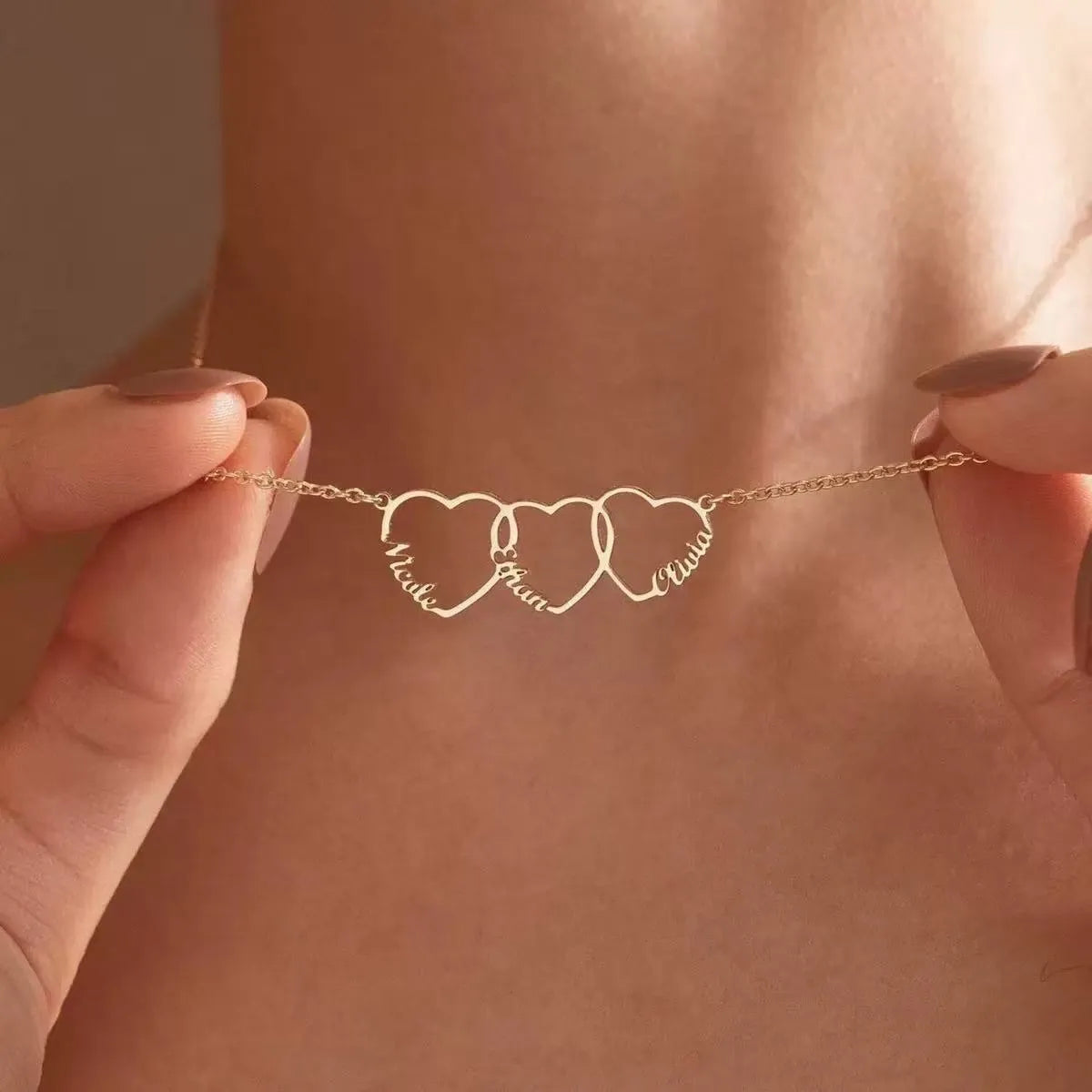A model wearing the Custom Heart Stack necklace featuring three interlocking hearts engraved with names in 18K gold.