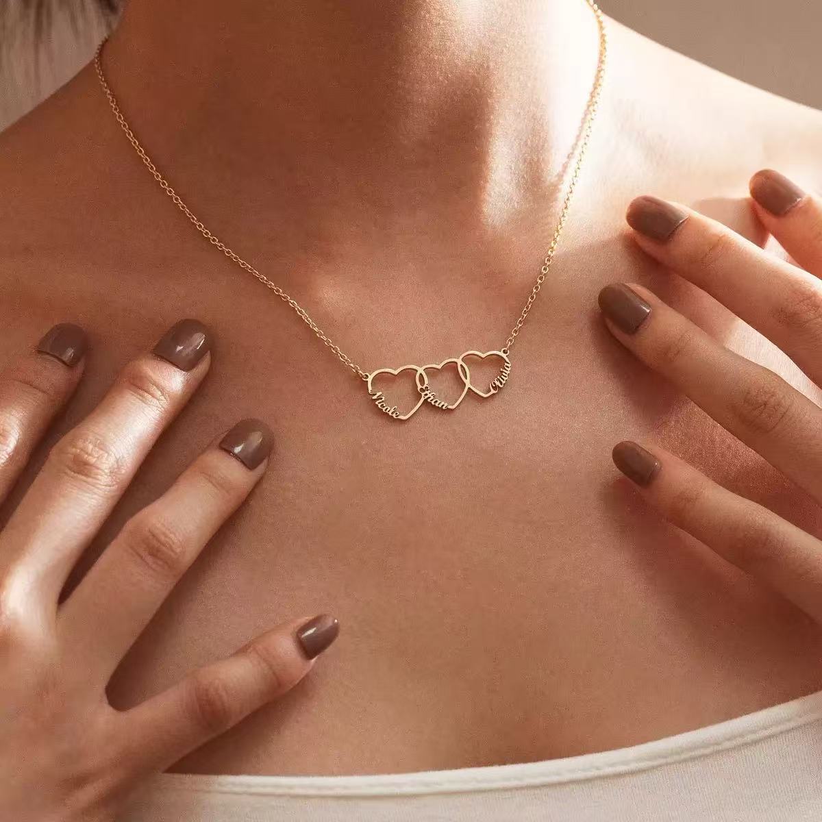 A model wearing the Custom Heart Stack necklace featuring three interlocking hearts engraved with names in 18K gold.