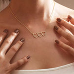A model wearing the Custom Heart Stack necklace featuring three interlocking hearts engraved with names in 18K gold.