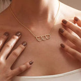 A model wearing the Custom Heart Stack necklace featuring three interlocking hearts engraved with names in 18K gold.