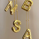 A collection of shiny 18K gold 3D balloon letter necklaces including N, B, S, and A, hanging elegantly to showcase the personalized alphabet jewelry collection.