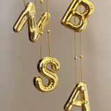 A collection of shiny 18K gold 3D balloon letter necklaces including N, B, S, and A, hanging elegantly to showcase the personalized alphabet jewelry collection.