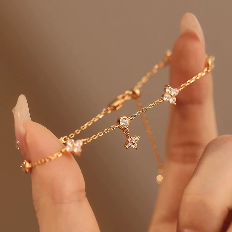 Close-up of a delicate 14K rose gold plated flower charm bracelet held between fingers, highlighting the playfully dangling clover design.