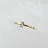 A delicate gold ring with a clear rectangular emerald-cut stone set horizontally, laid flat on soft white tulle fabric.