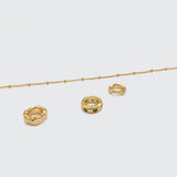 A deconstructed view of the Emerald Trio Ring Necklace, showing the 18K gold-plated satellite chain and three distinct rings: hammered, smooth, and emerald-studded.