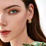 Close-up of a woman looking slightly off-camera, wearing a green floral top and a chunky braided gold hoop earring.