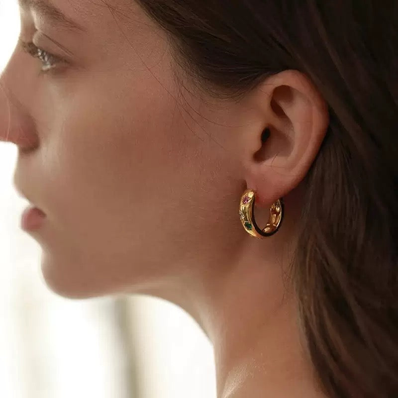 A stylish model showcasing a pair of vibrant rainbow gemstone huggie earrings, highlighting their bold and modern design.