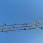 Detailed view of the geometric crystals on the 18K gold plated chain held against a clear blue sky.