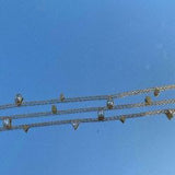 Detailed view of the geometric crystals on the 18K gold plated chain held against a clear blue sky.
