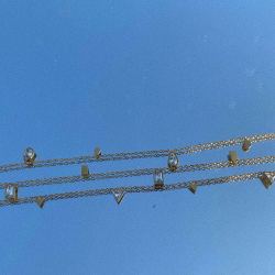 Detailed view of the geometric crystals on the 18K gold plated chain held against a clear blue sky.