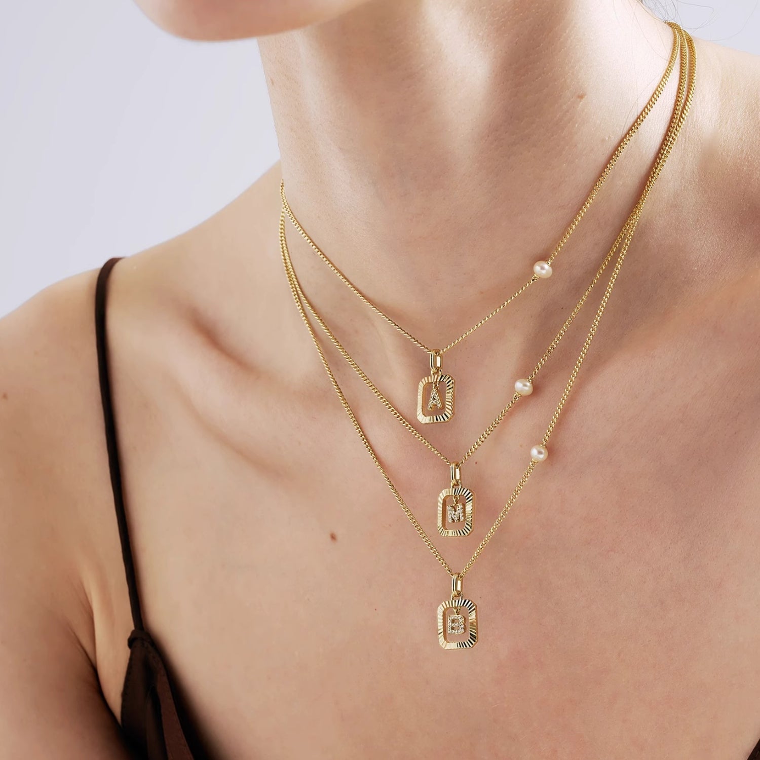 Close-up of the 14K gold plated vintage initial necklace resting on a woman's collarbone, highlighting the asymmetrical pearl and ribbed frame.