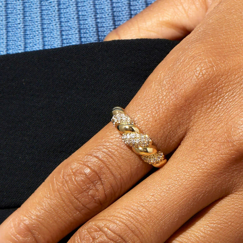 Macro view of a gold-plated pavé twist ring on a finger, emphasizing the brilliant-cut stones and craftsmanship.