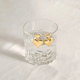 Two gold plated double puffy heart dangle earrings elegantly hanging on the rim of a clear textured glass.