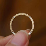 Macro view of a gold promise ring resting on a fingertip, highlighting the textured wheat motif and matte brushed finish.