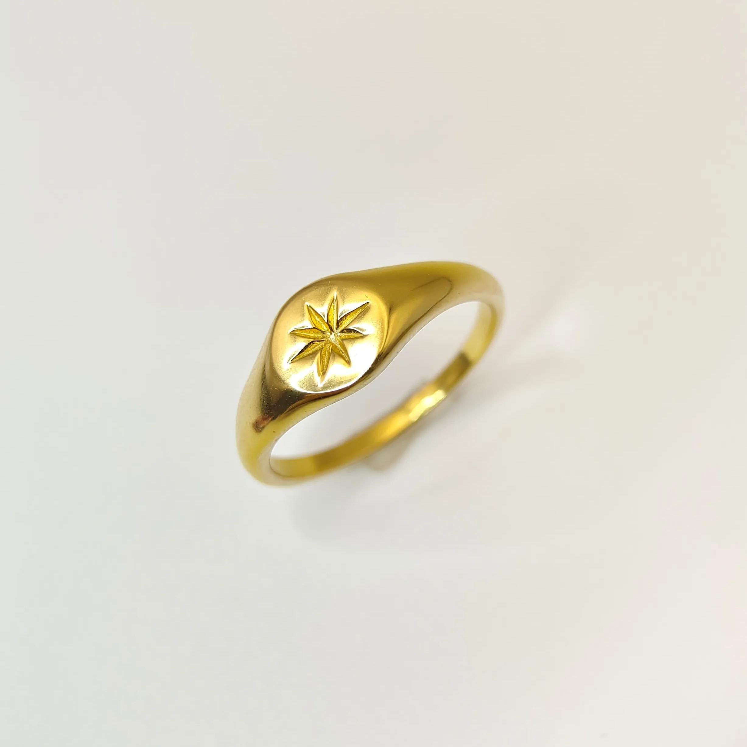 Angled view of a minimalist gold signet ring showcasing its polished surface and an engraved starburst pattern, resting on a white surface.