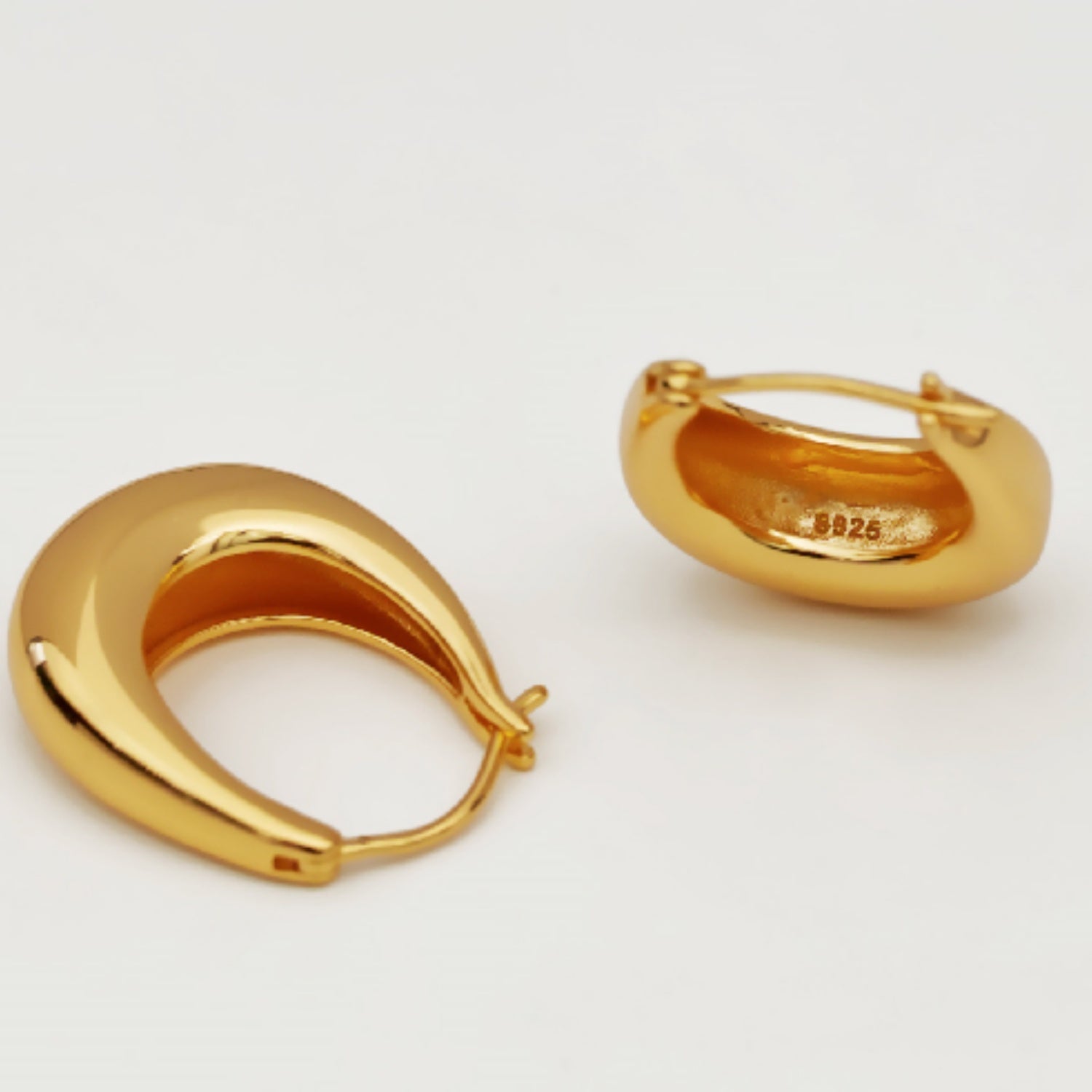 Two gold-plated horseshoe-shaped hoop earrings lying flat on a white surface.