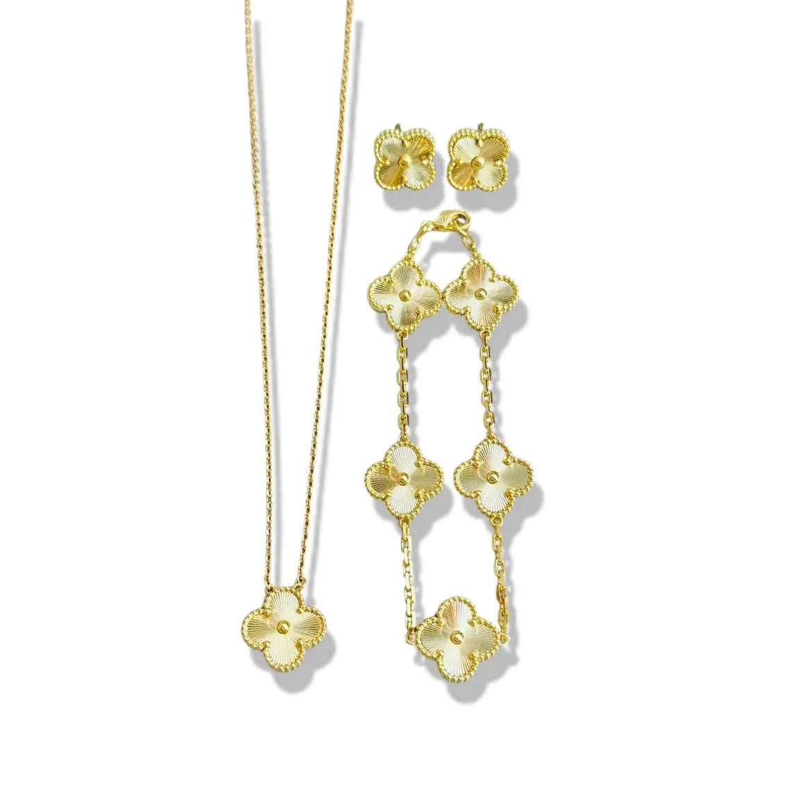 An elegant 18K gold plated jewelry set featuring a black four-leaf clover necklace, matching bracelet, and stud earrings laid on a white background.