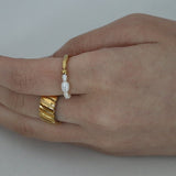 Close-up of a hand wearing a thick gold ribbed band ring paired next to a delicate gold ring featuring small white pearls.