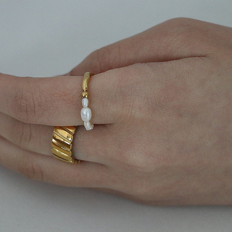 Close-up of a hand wearing a thick gold ribbed band ring paired next to a delicate gold ring featuring small white pearls.
