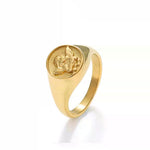 A gold signet ring featuring a raised, embossed angel or cherub design, isolated on a clean white background.