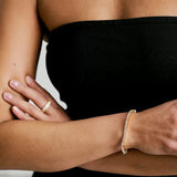 Close-up of a model's arm wearing a classic gold tennis bracelet, styled with a black strapless evening dress.