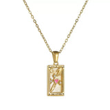 A gold rectangular tarot card pendant labeled THE LOVERS, featuring a white enamel background, gold hands reaching towards a central pink heart accented with clear stones.
