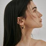 A close-up of a model wearing the chunky 18K gold plated U-shape hoop earrings, showcasing the sculptural design.