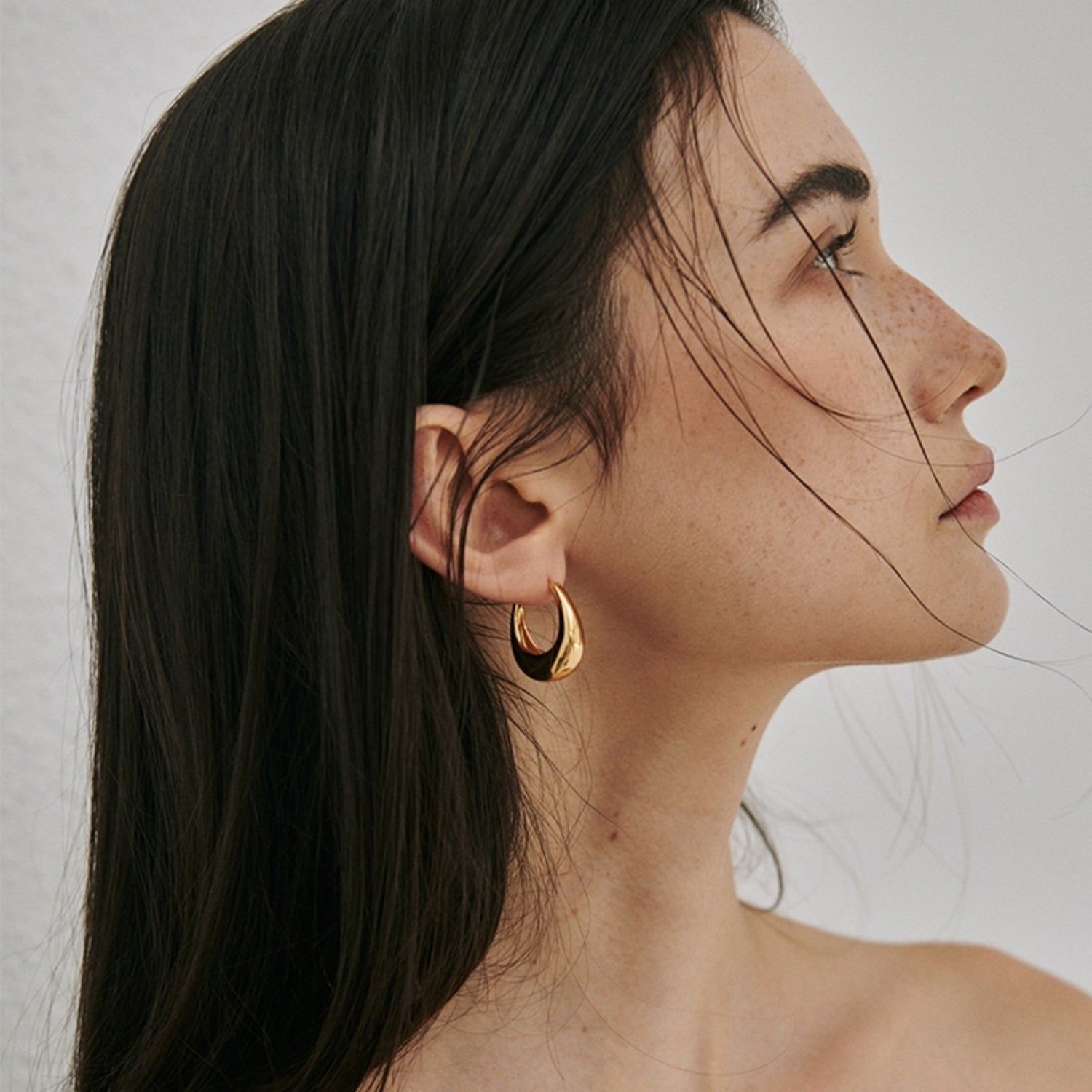 A close-up of a model wearing the chunky 18K gold plated U-shape hoop earrings, showcasing the sculptural design.