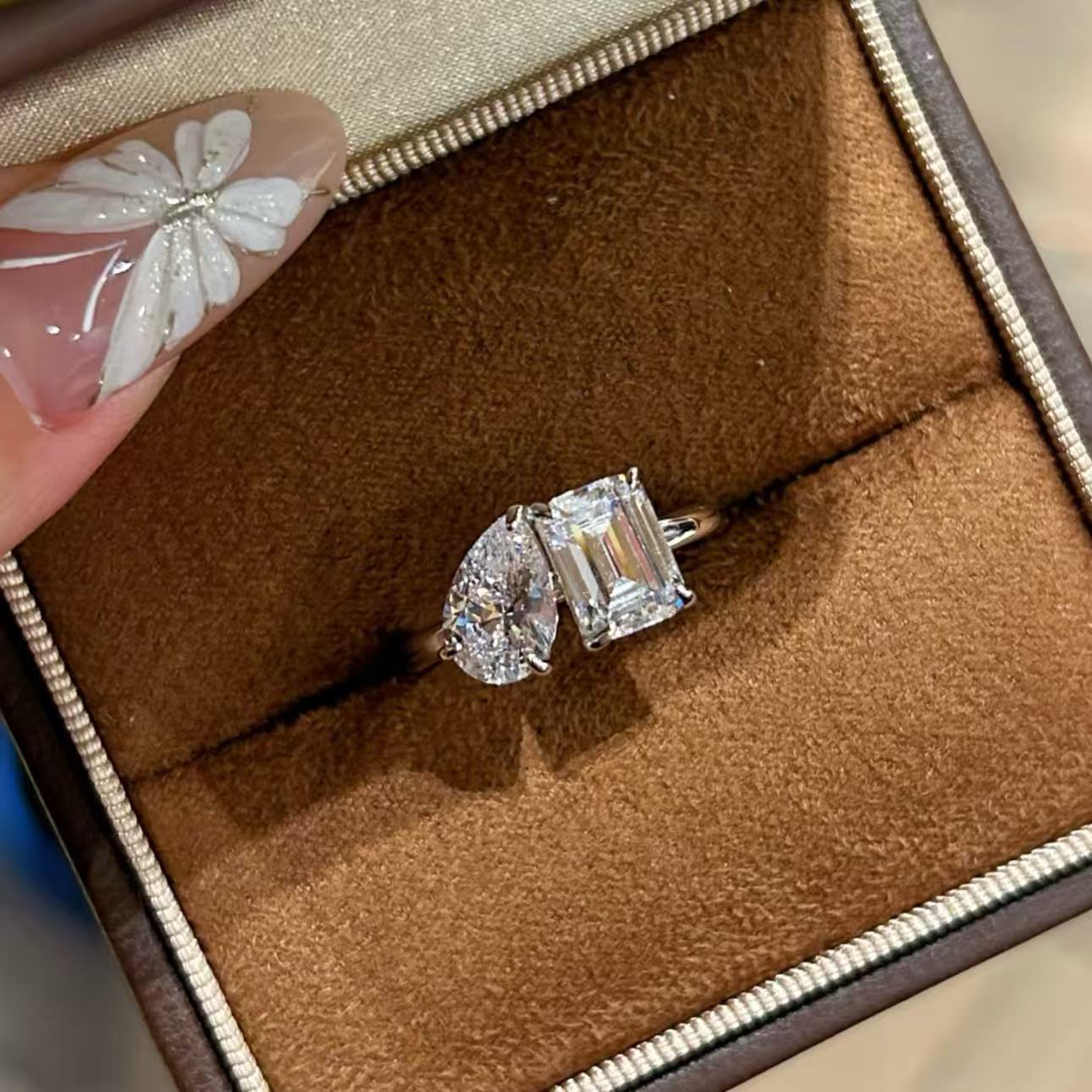 Close-up shot of the sparkling 1.5ct emerald and 1.5ct pear cut high-carbon diamonds on the Toi et Moi ring resting in a box.