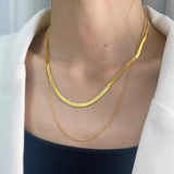 A woman wearing a white blazer styled with the layered gold herringbone and snake chain necklace