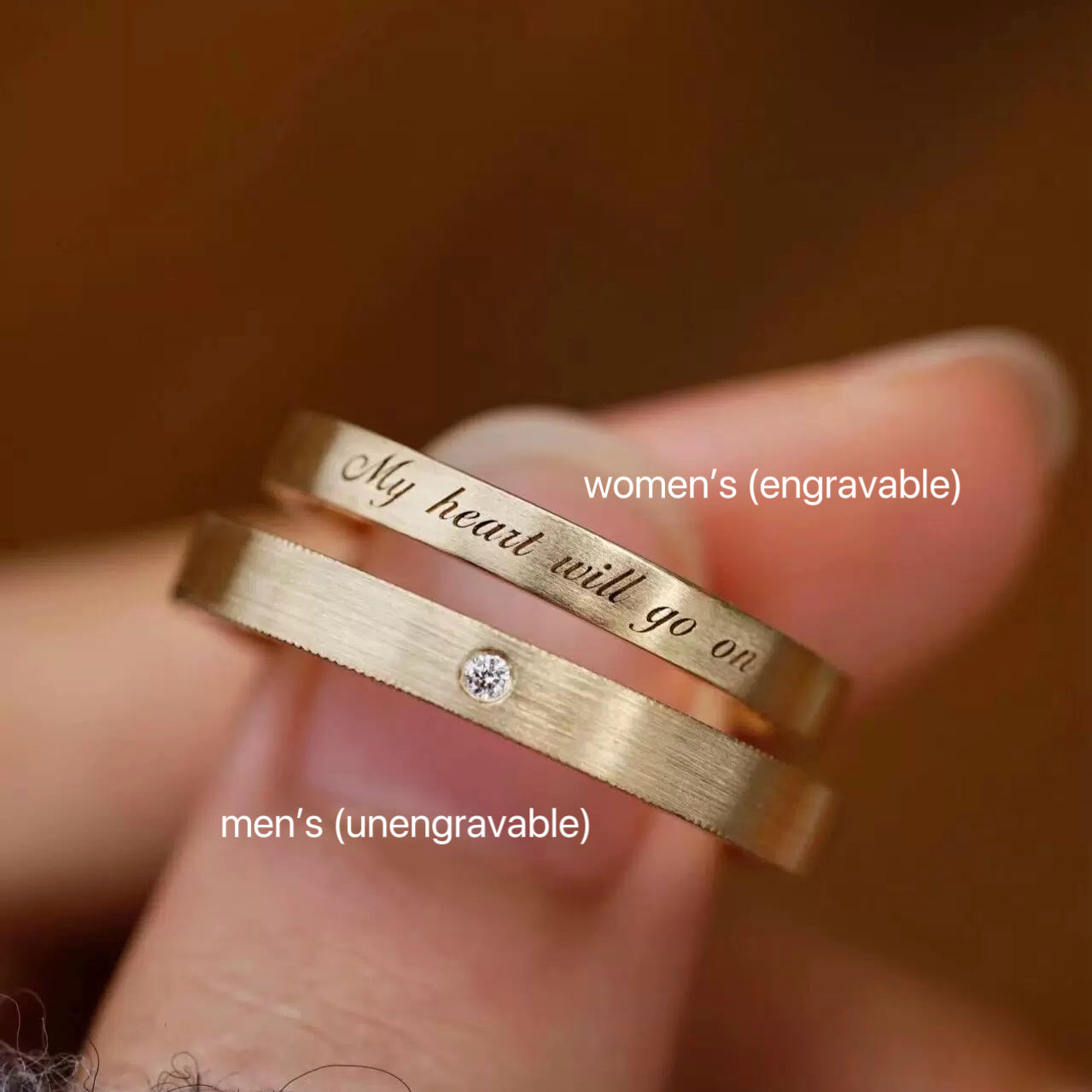 Fingers holding a set of his and hers gold promise rings, specifically highlighting the engravable women's ring and the unengravable single-stone men's ring.