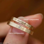 Fingers holding a set of his and hers gold promise rings, specifically highlighting the engravable women's ring and the unengravable single-stone men's ring.