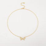 A delicate 18K gold plated cable chain necklace featuring a sparkling cubic zirconia ribbon bow pendant, laid flat against a white surface.